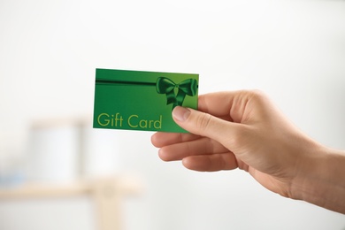 Photo of Woman holding gift card on blurred background, closeup