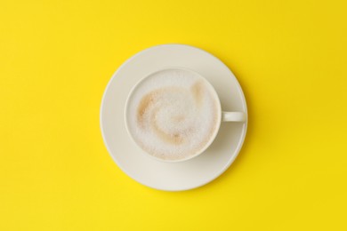 Photo of Tasty cappuccino in coffee cup on yellow background, top view
