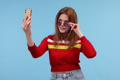 Photo of Beautiful woman in sunglasses taking selfie on light blue background