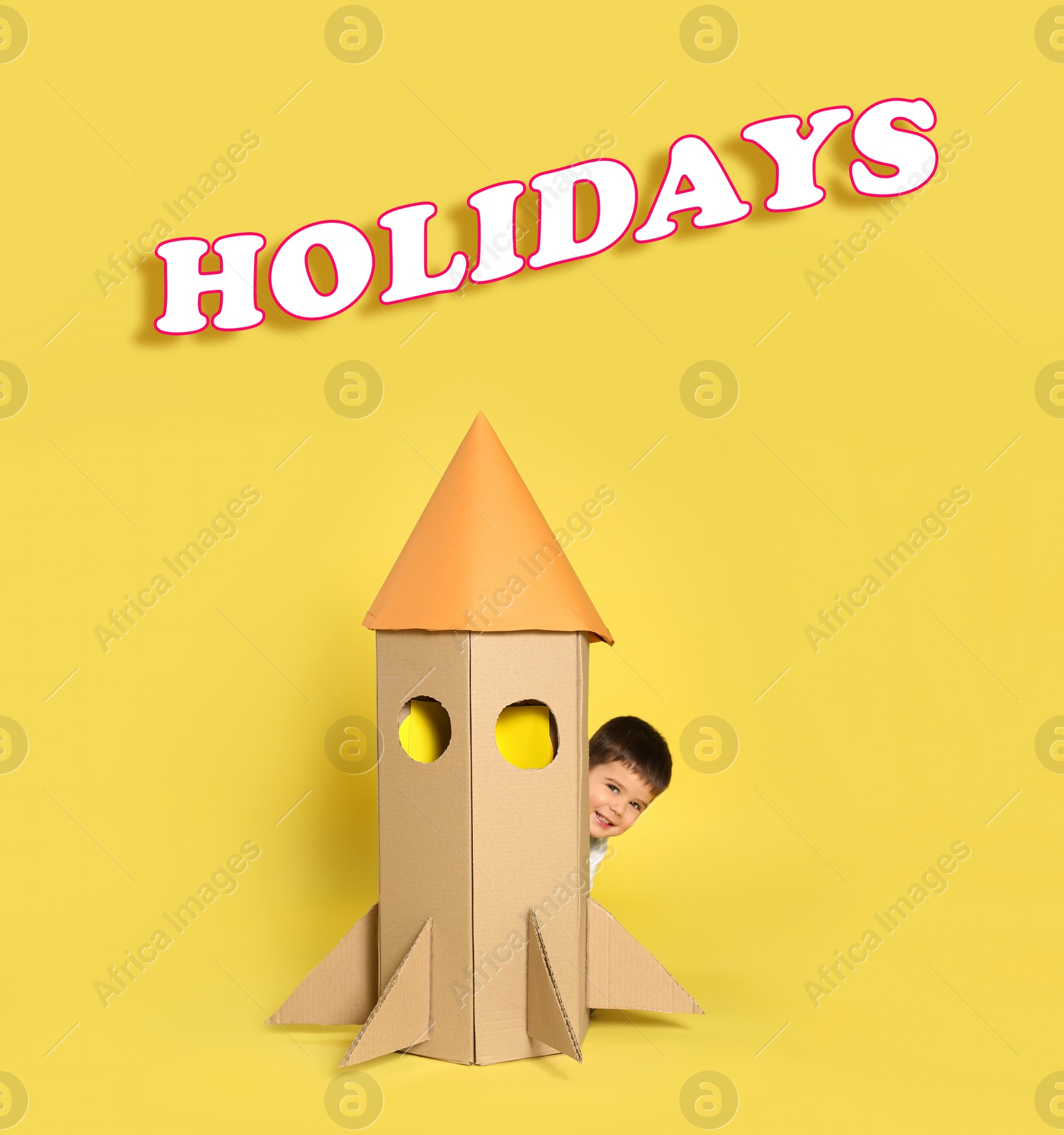 Image of School holidays. Cute little child playing with cardboard rocket near yellow wall