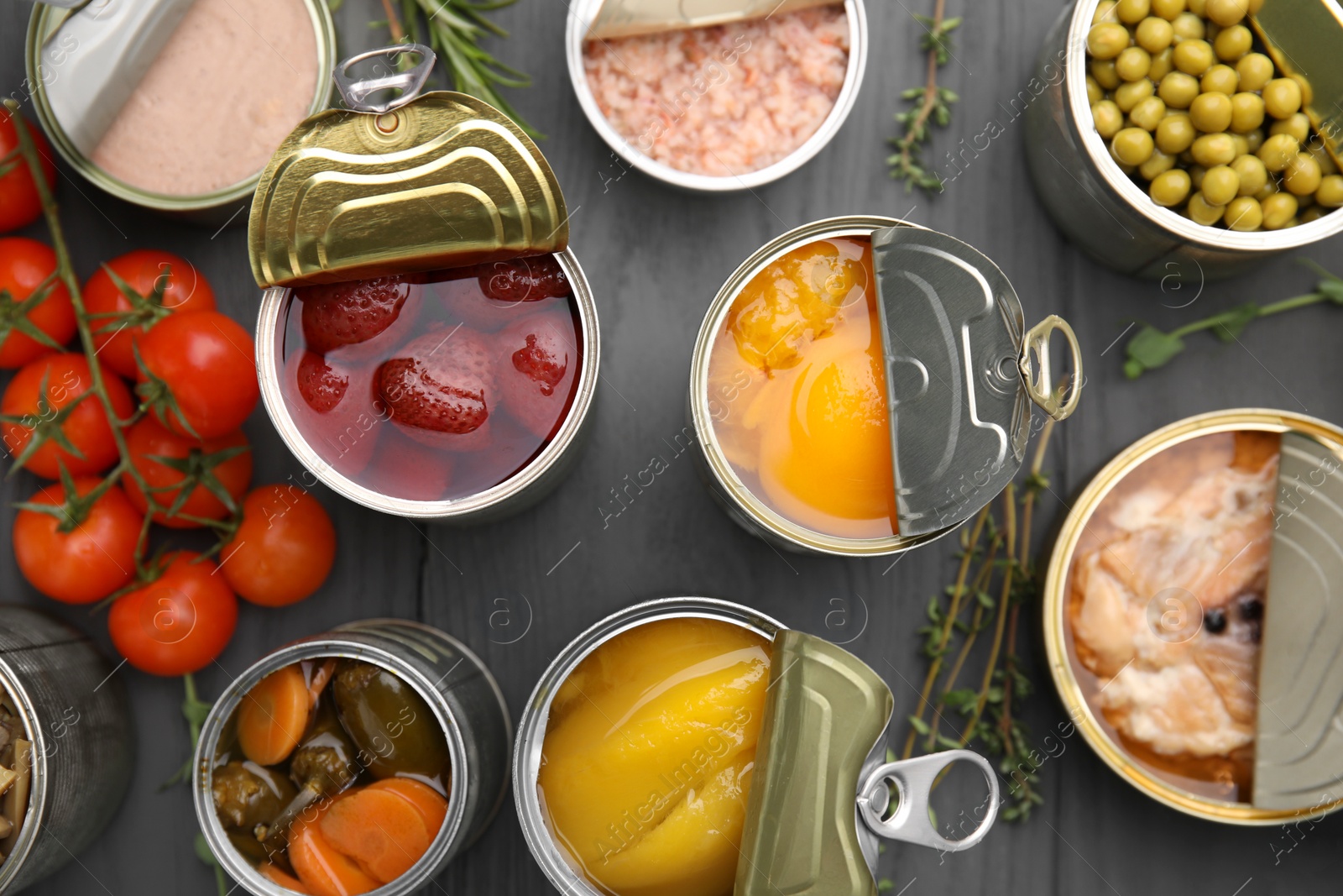 Photo of Open tin cans with different products on gray wooden table, flat lay