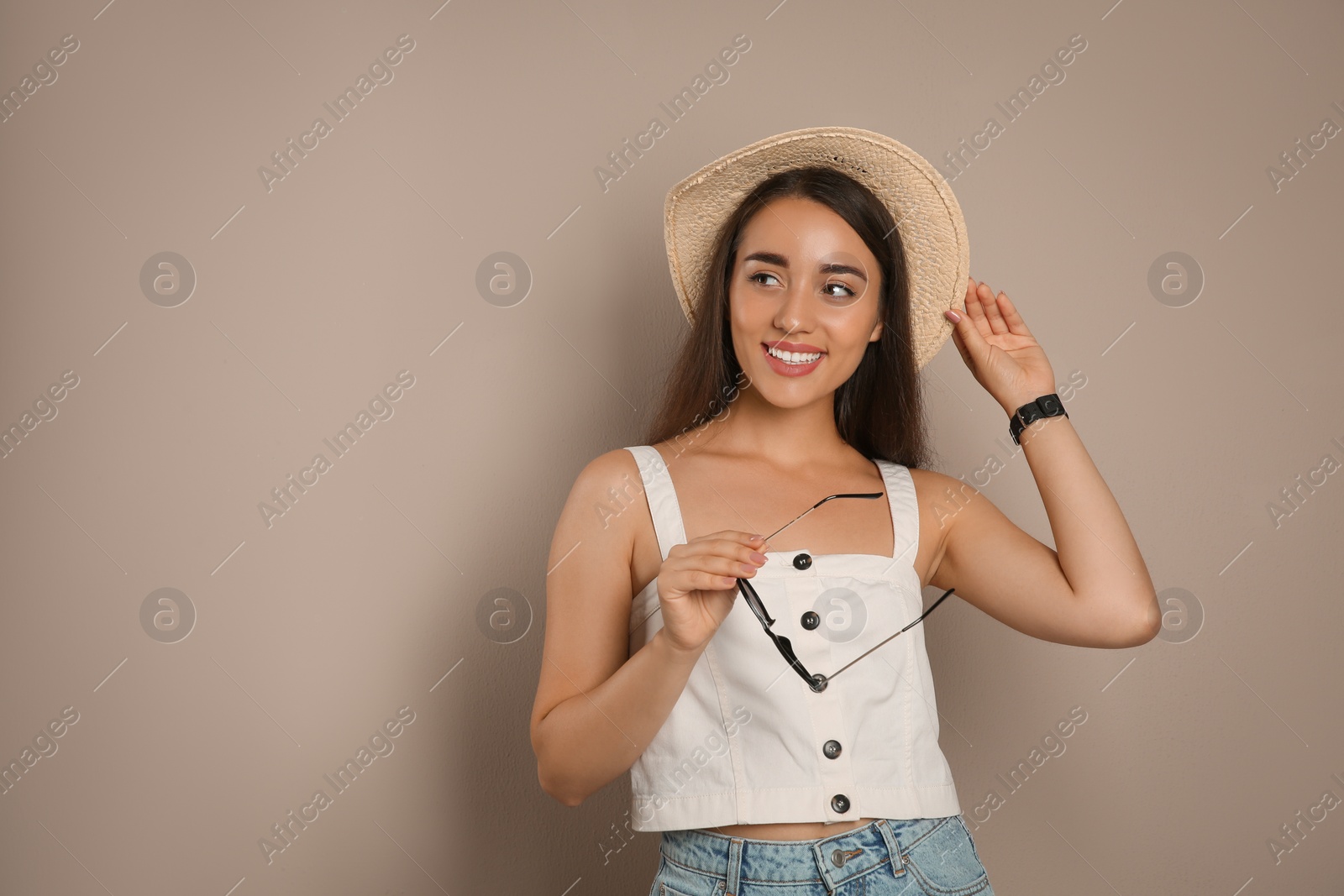 Photo of Beautiful young woman with straw hat and sunglasses on beige background, space for text. Stylish headdress