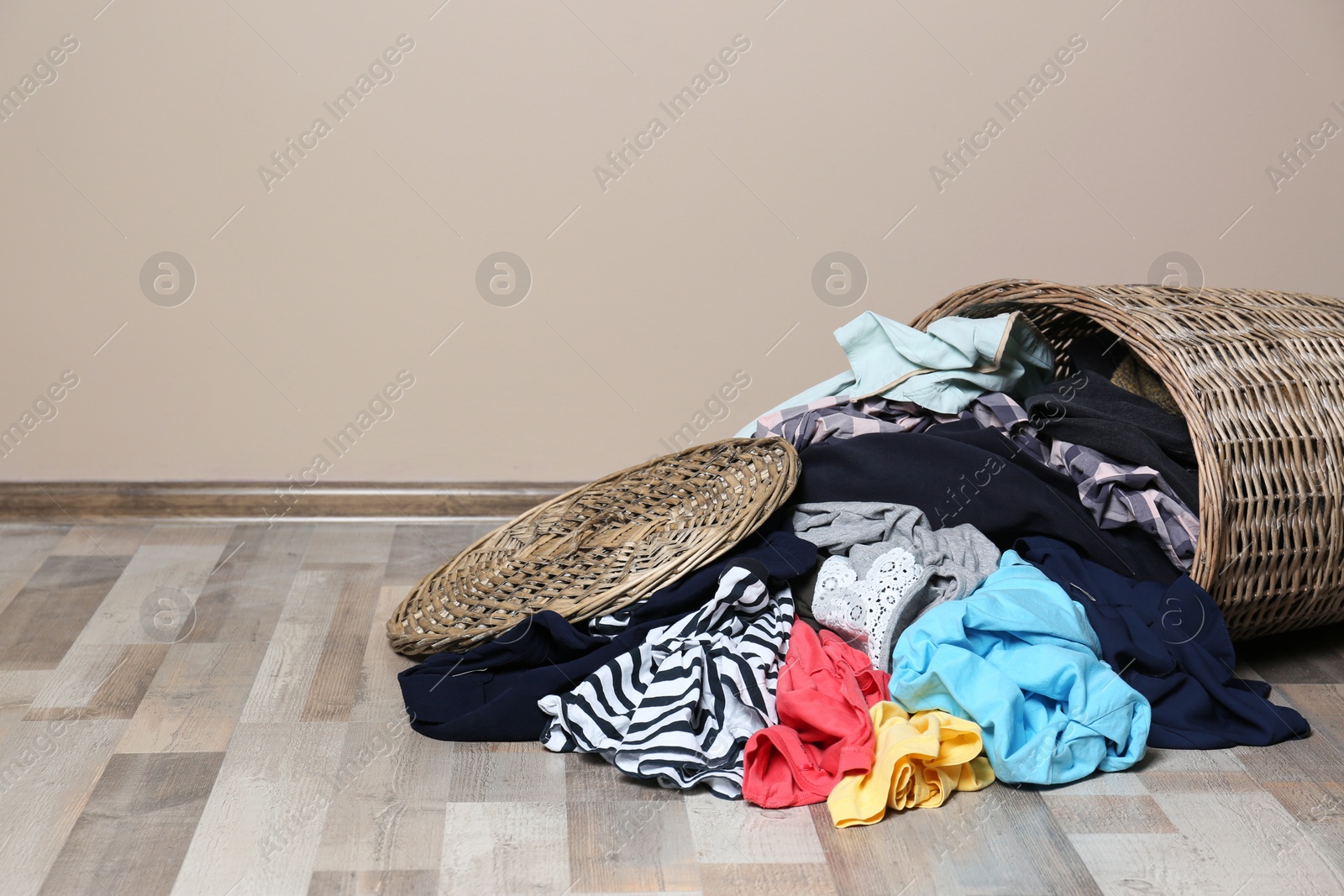 Photo of Dirty clothes scattered from laundry basket on floor indoors. Space for text