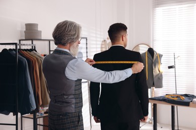 Photo of Professional tailor working with client in atelier, back view