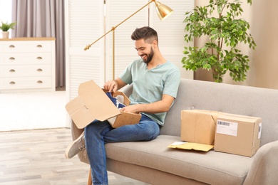 Young man opening parcel with shoes on sofa at home
