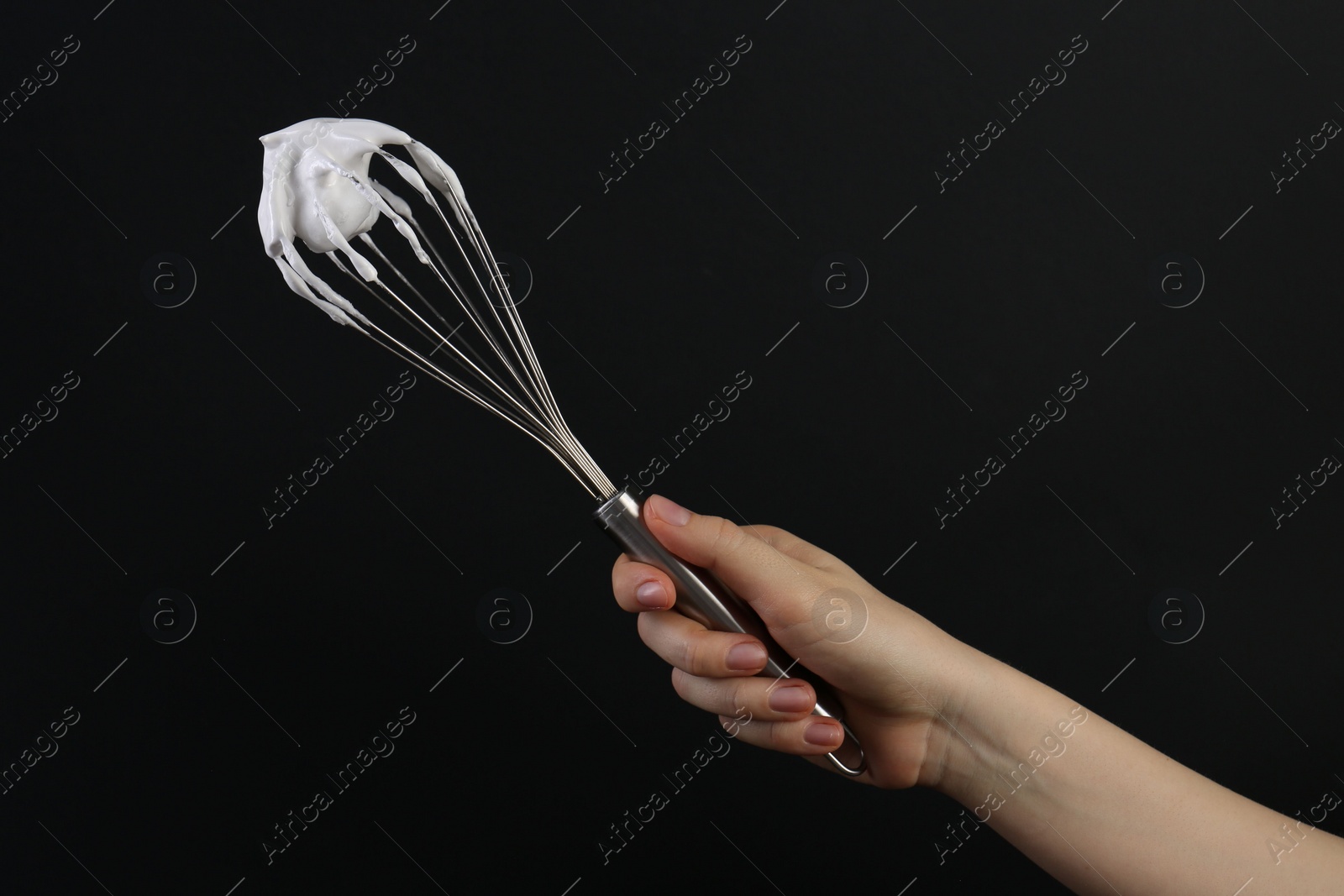 Photo of Woman holding whisk with whipped cream on black background, closeup