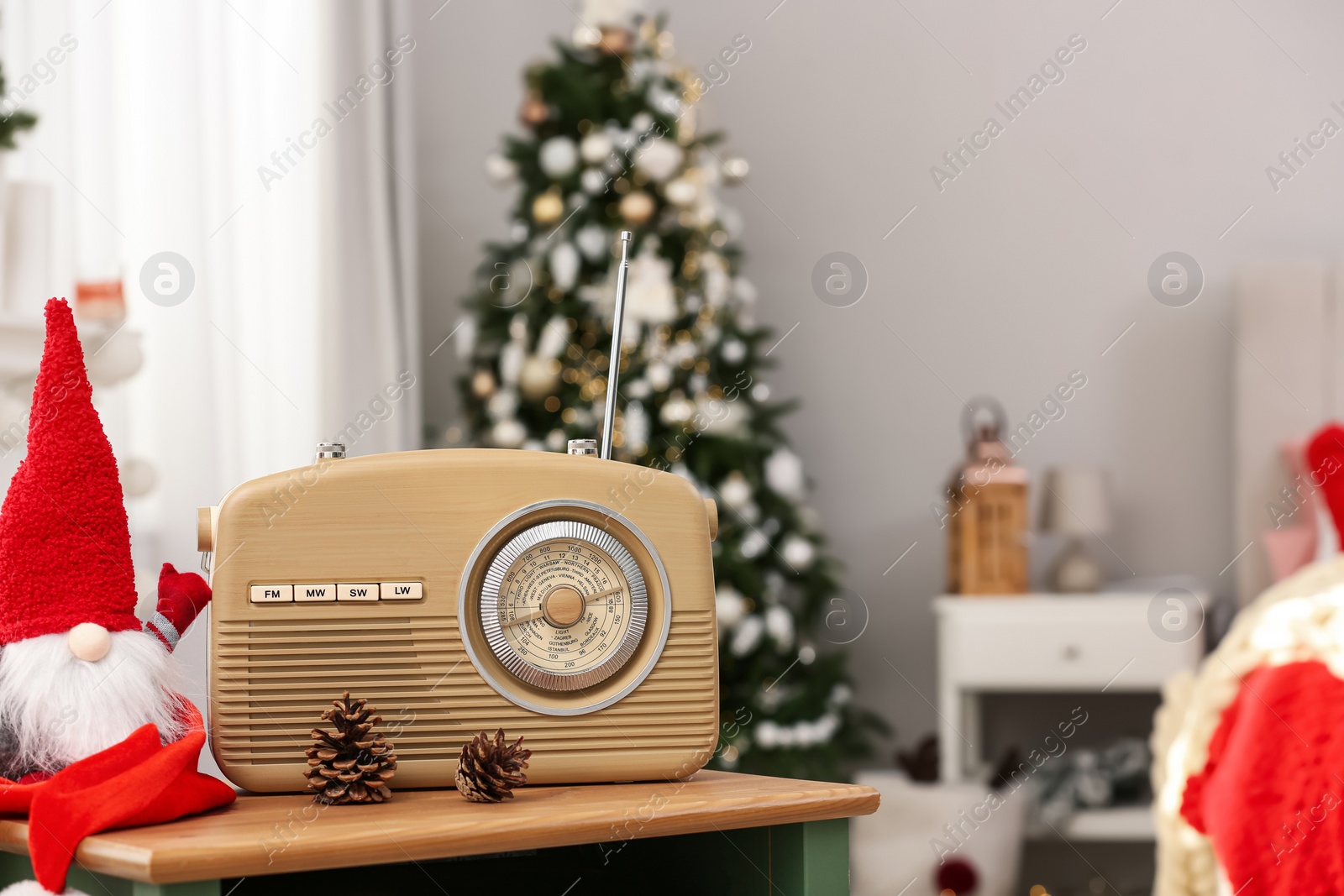 Photo of Stylish radio and Christmas gnome on wooden table in decorated room. Space for text