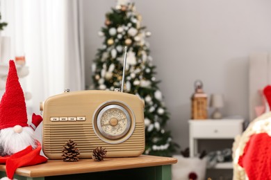 Photo of Stylish radio and Christmas gnome on wooden table in decorated room. Space for text