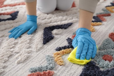 Photo of Woman in rubber gloves cleaning carpet with rag indoors, closeup