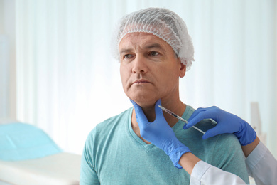 Photo of Mature man with double chin receiving injection in clinic