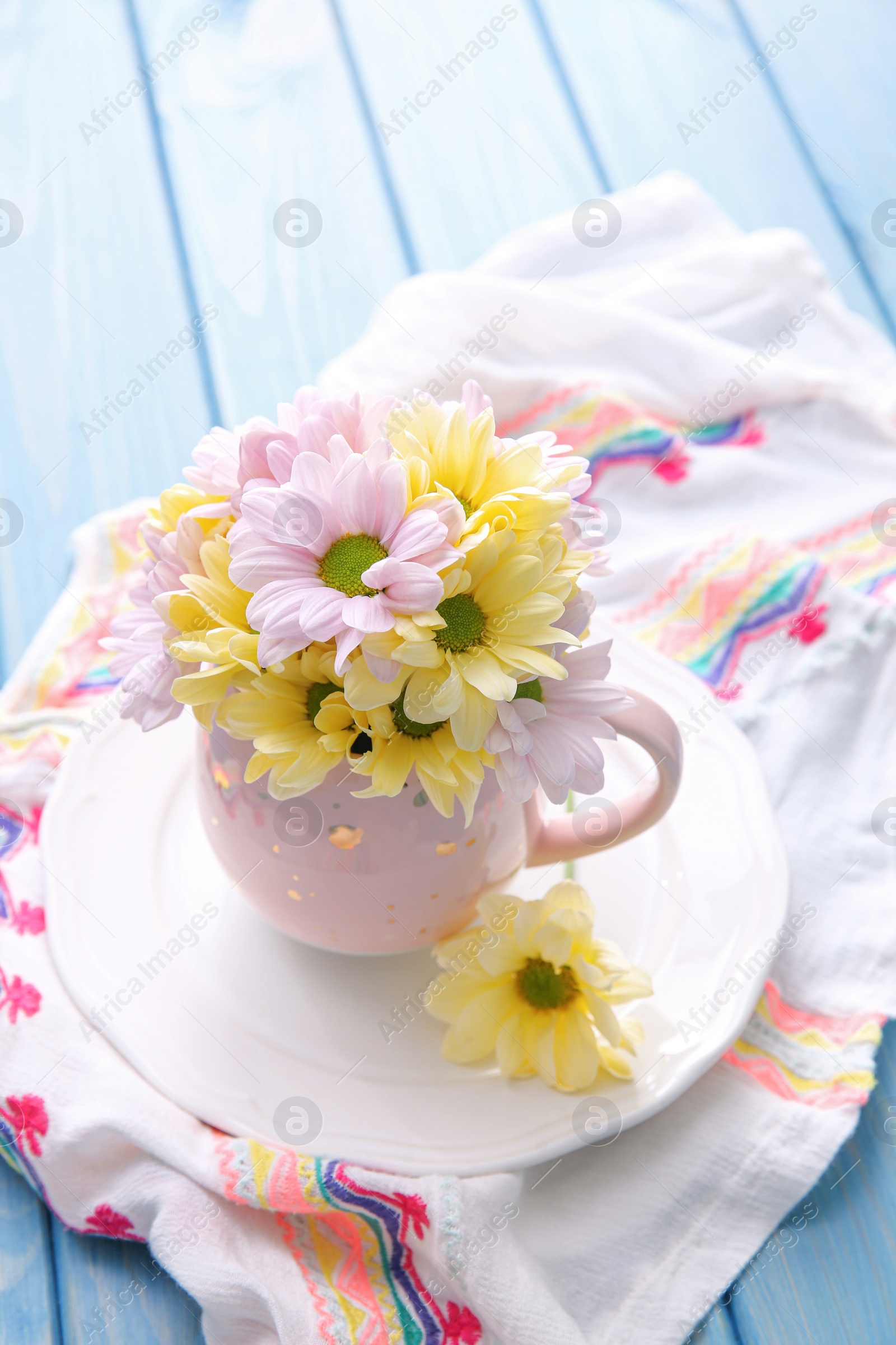 Photo of Bouquet of beautiful flowers in cup on light blue wooden table