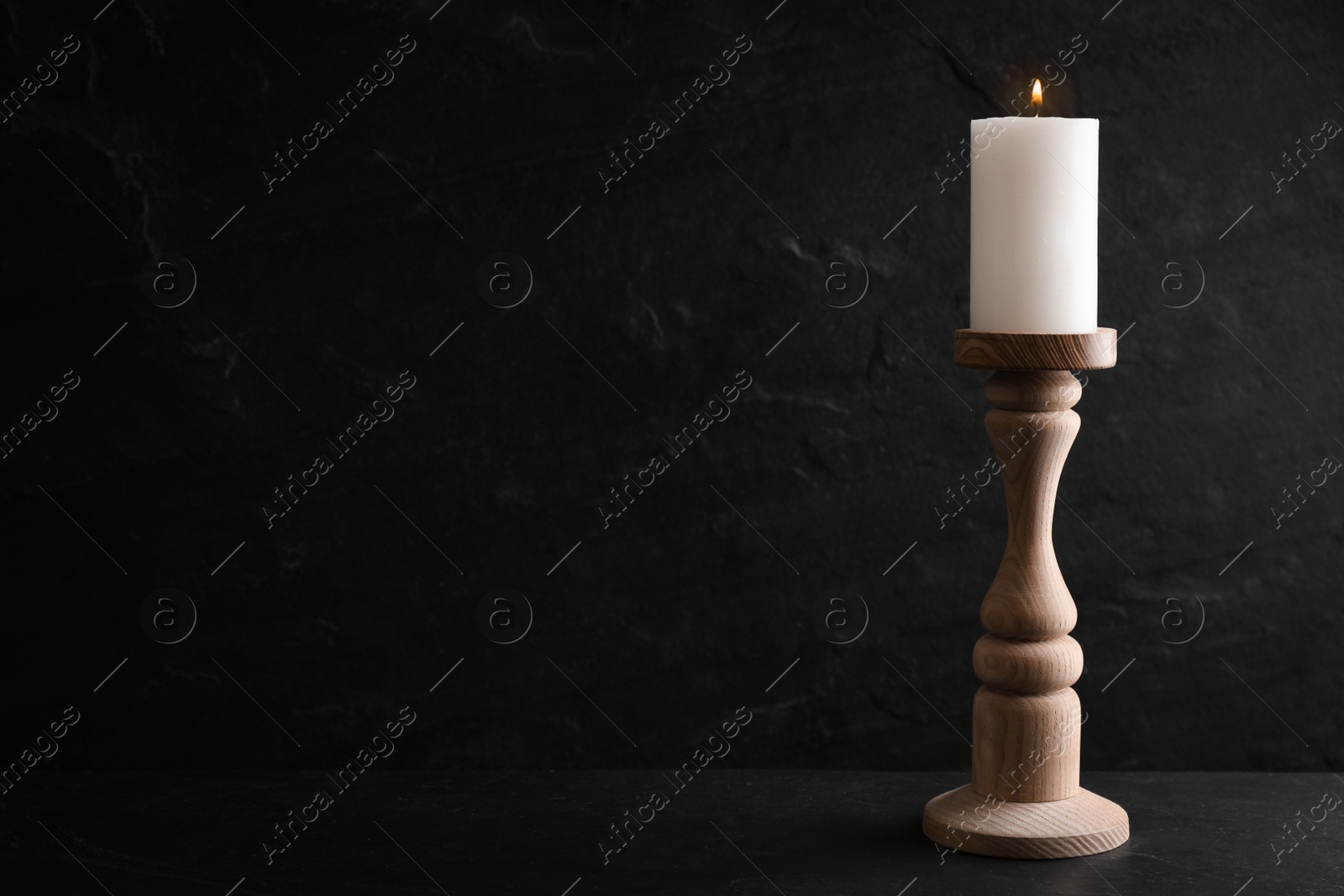 Photo of Elegant candlestick with burning candle on black table. Space for text