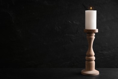 Elegant candlestick with burning candle on black table. Space for text