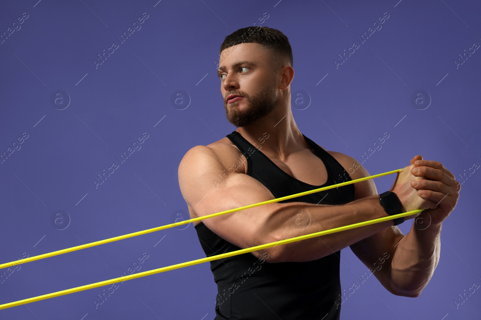 Photo of Muscular man exercising with elastic resistance band on purple background