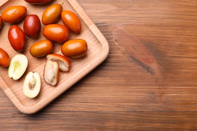 Photo of Wooden plate with fresh Ziziphus jujuba fruits on table, top view. Space for text