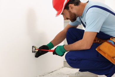 Electrician with screwdriver repairing power socket indoors