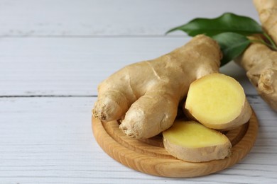 Cut and whole fresh ginger with leaves on white wooden table. Space for text