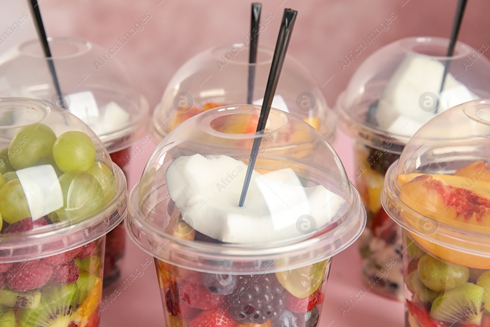 Photo of Fresh tasty fruit salad in plastic cups on pink background, closeup