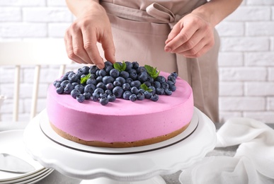 Photo of Young woman decorating tasty blueberry cake with mint at table, closeup