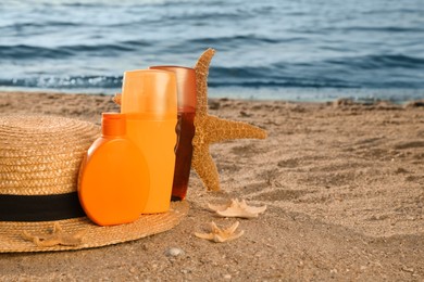 Sun protection products, hat and starfishes on sand near sea, space for text