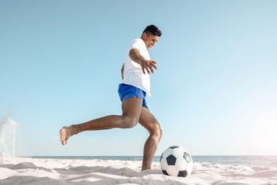 Man kicking football ball on beach near sea