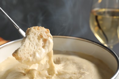 Photo of Dipping piece of bread into fondue pot with melted cheese on grey background, closeup