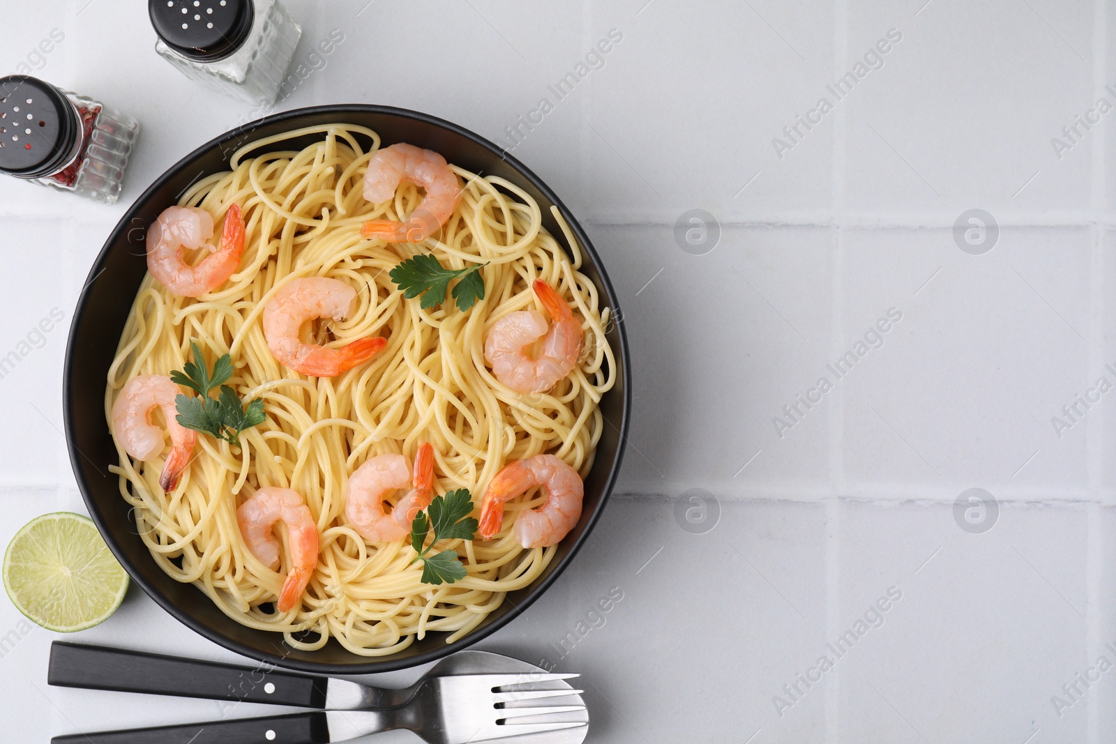 Photo of Tasty spaghetti with shrimps and parsley in bowl served on light tiled table, flat lay. Space for text