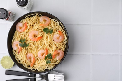 Tasty spaghetti with shrimps and parsley in bowl served on light tiled table, flat lay. Space for text