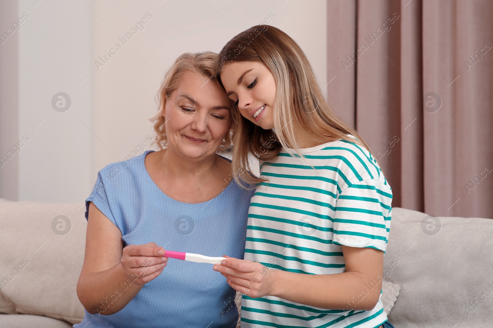 Photo of Young woman showing her mother pregnancy test at home. Grandparent reaction to future grandson
