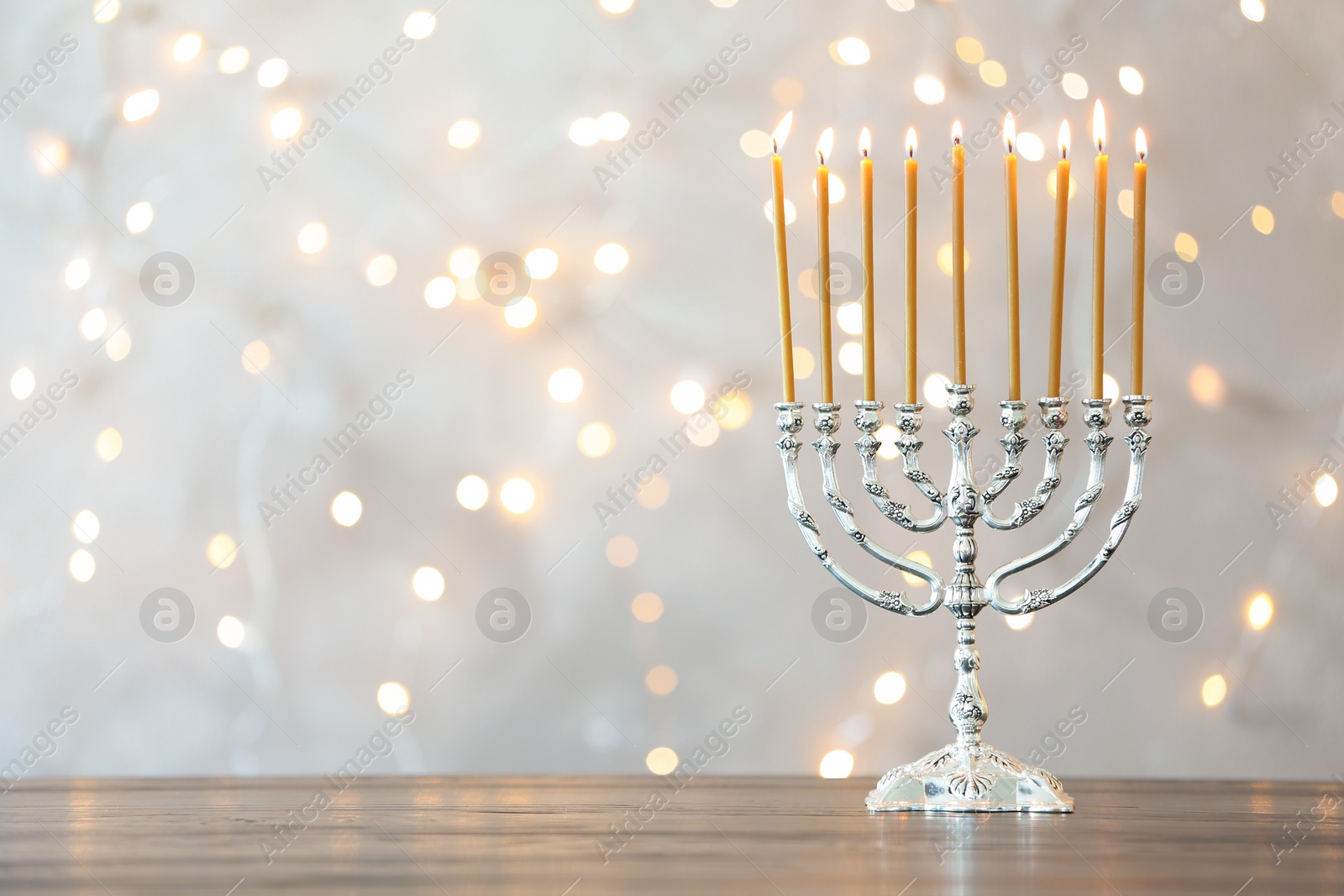 Photo of Hanukkah menorah with candles on table against blurred lights