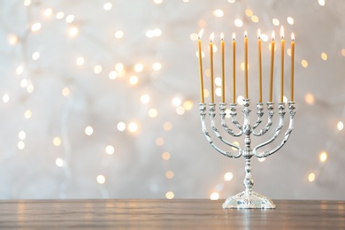 Photo of Hanukkah menorah with candles on table against blurred lights