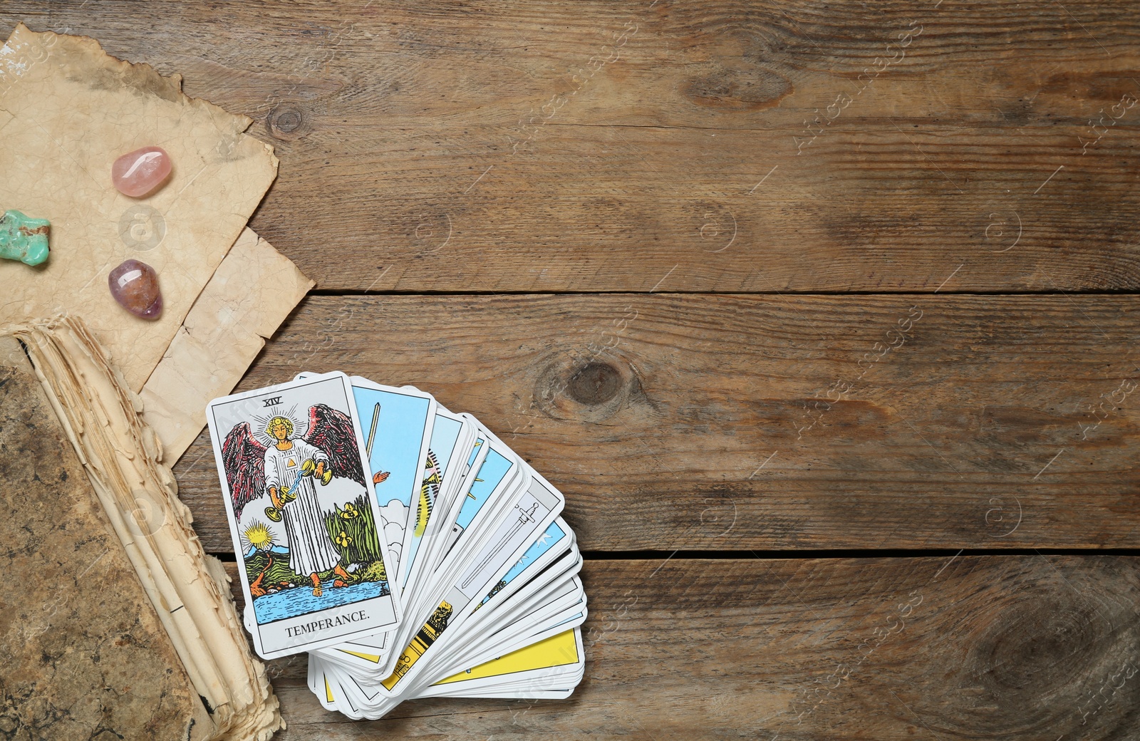 Photo of Tarot cards, old book and crystals on wooden table, flat lay