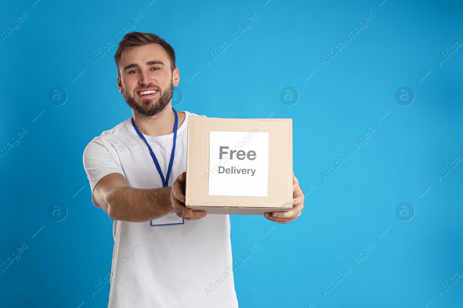 Photo of Male courier holding parcel with sticker Free Delivery on light blue background