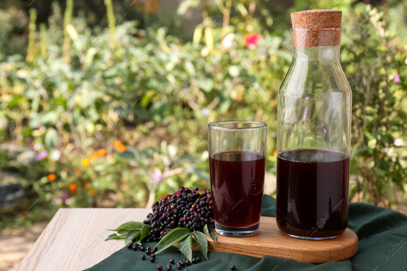 Photo of Elderberry drink and Sambucus berries on table outdoors, space for text
