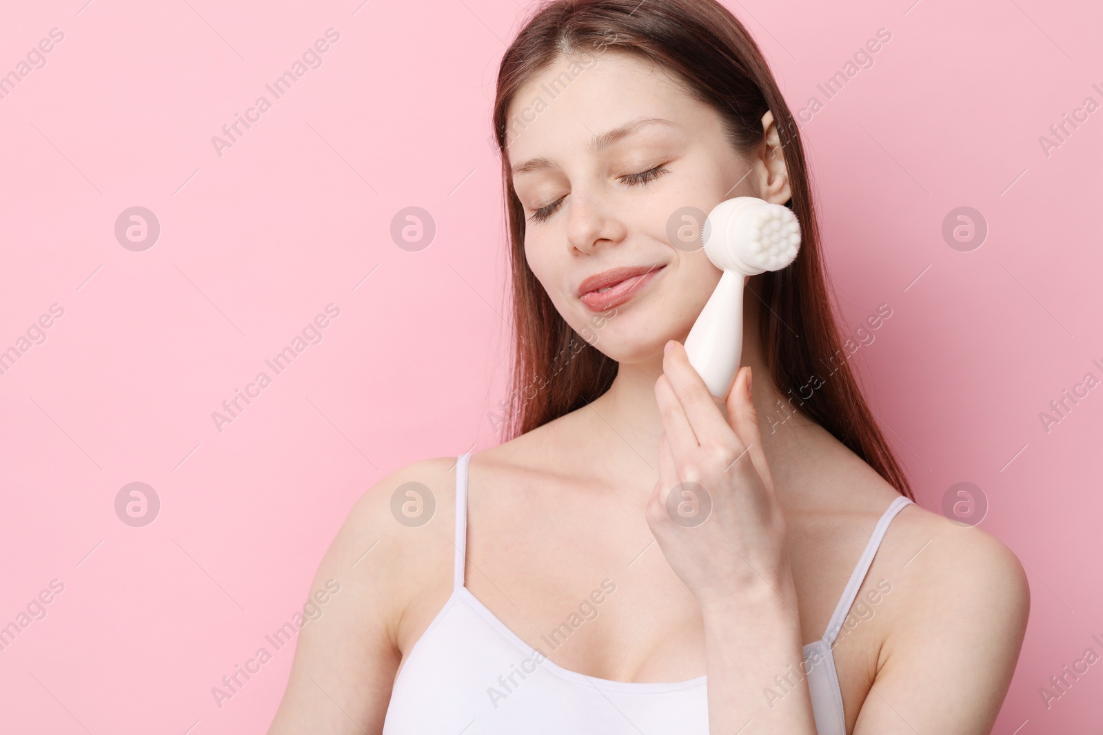 Photo of Washing face. Young woman with cleansing brush on pink background, space for text