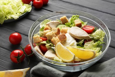 Photo of Bowl of delicious salad with Chinese cabbage, lemon, tomatoes and bread croutons on black wooden table