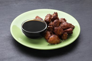 Tasty roasted meat served with soy sauce on dark grey table, closeup