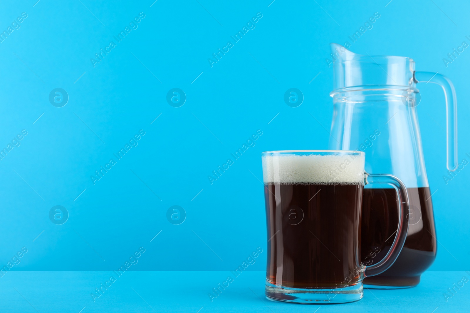 Photo of Delicious homemade kvass in glass mug and jug on light blue background. Space for text