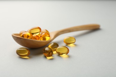 Vitamin capsules in wooden spoon on light grey background, closeup. Health supplement