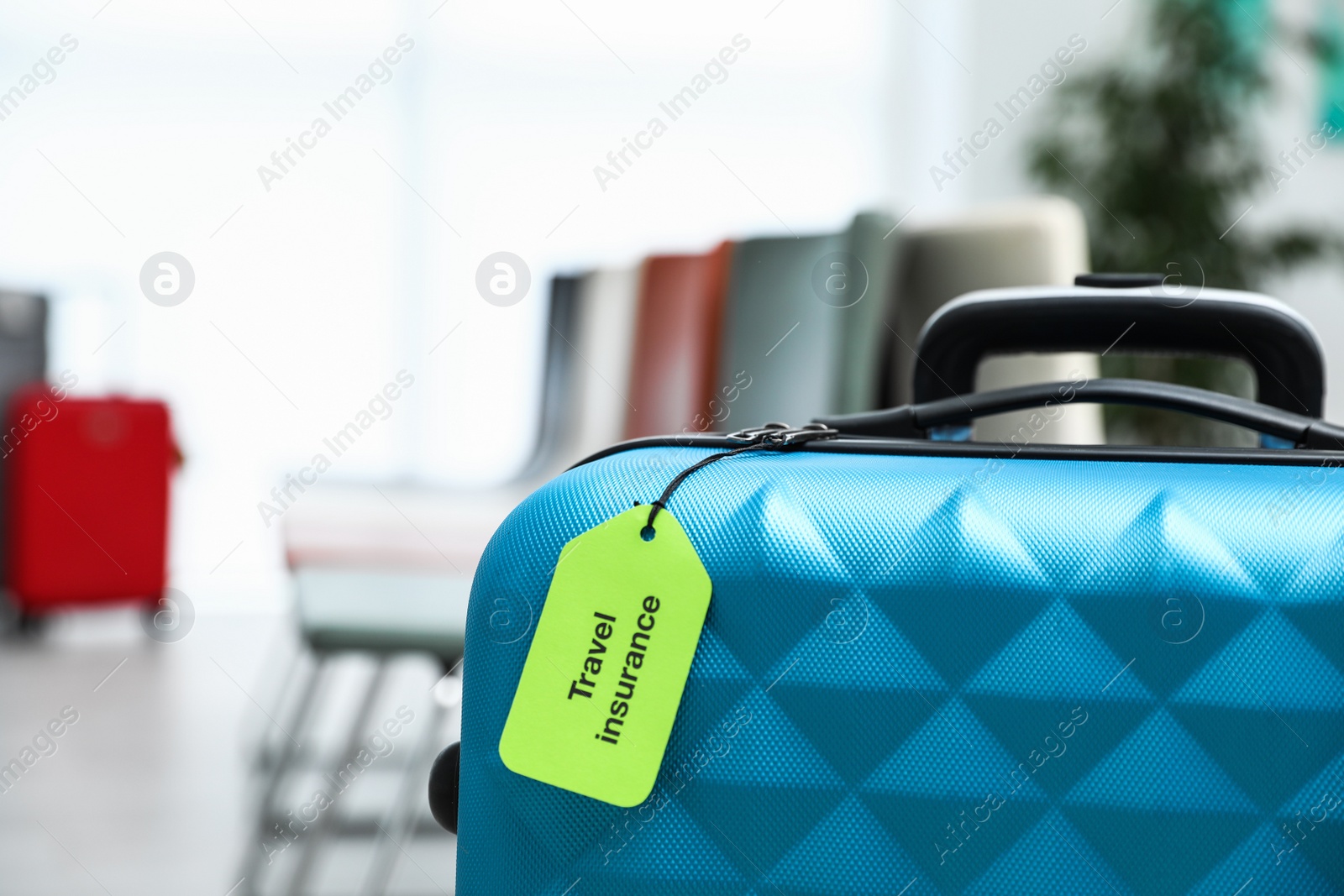Photo of Blue suitcase with TRAVEL INSURANCE label indoors, closeup. Space for text