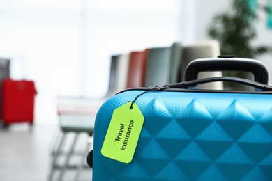 Blue suitcase with TRAVEL INSURANCE label indoors, closeup. Space for text