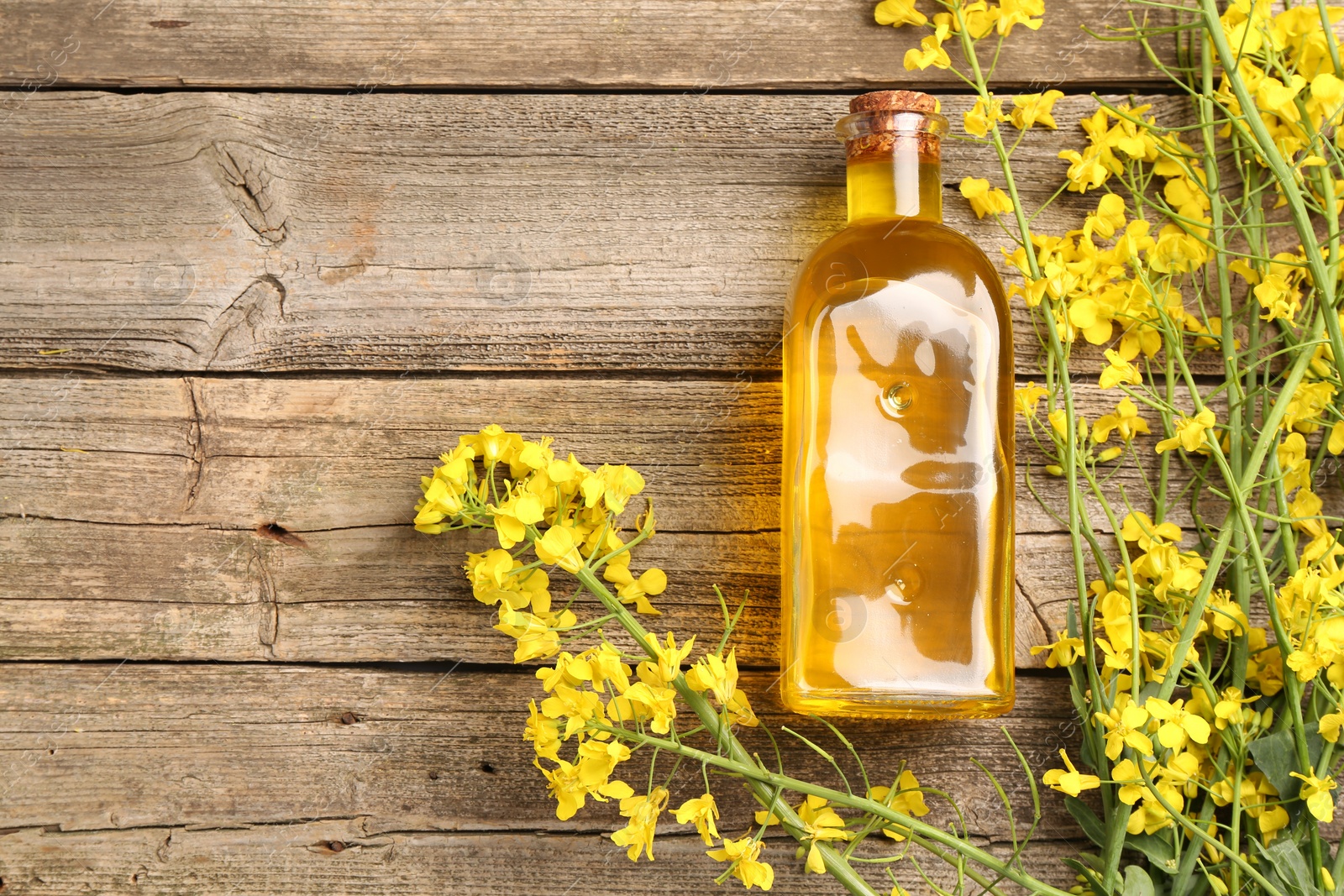 Photo of Rapeseed oil in glass bottle and beautiful yellow flowers on wooden table, flat lay. Space for text