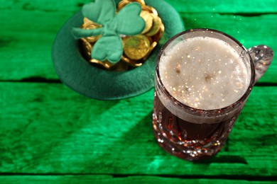 Image of St. Patrick's day. Beer, leprechaun hat with gold and decorative clover leaf on green wooden table. Space for text