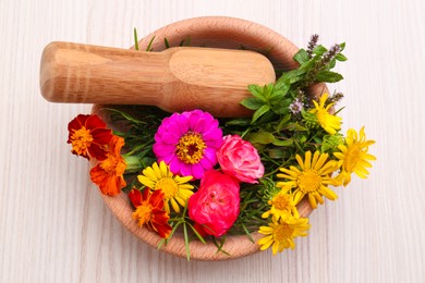 Mortar with pestle and beautiful fresh flowers on wooden table, top view