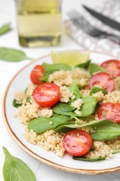 Delicious quinoa salad with tomatoes and spinach leaves served on white table, closeup