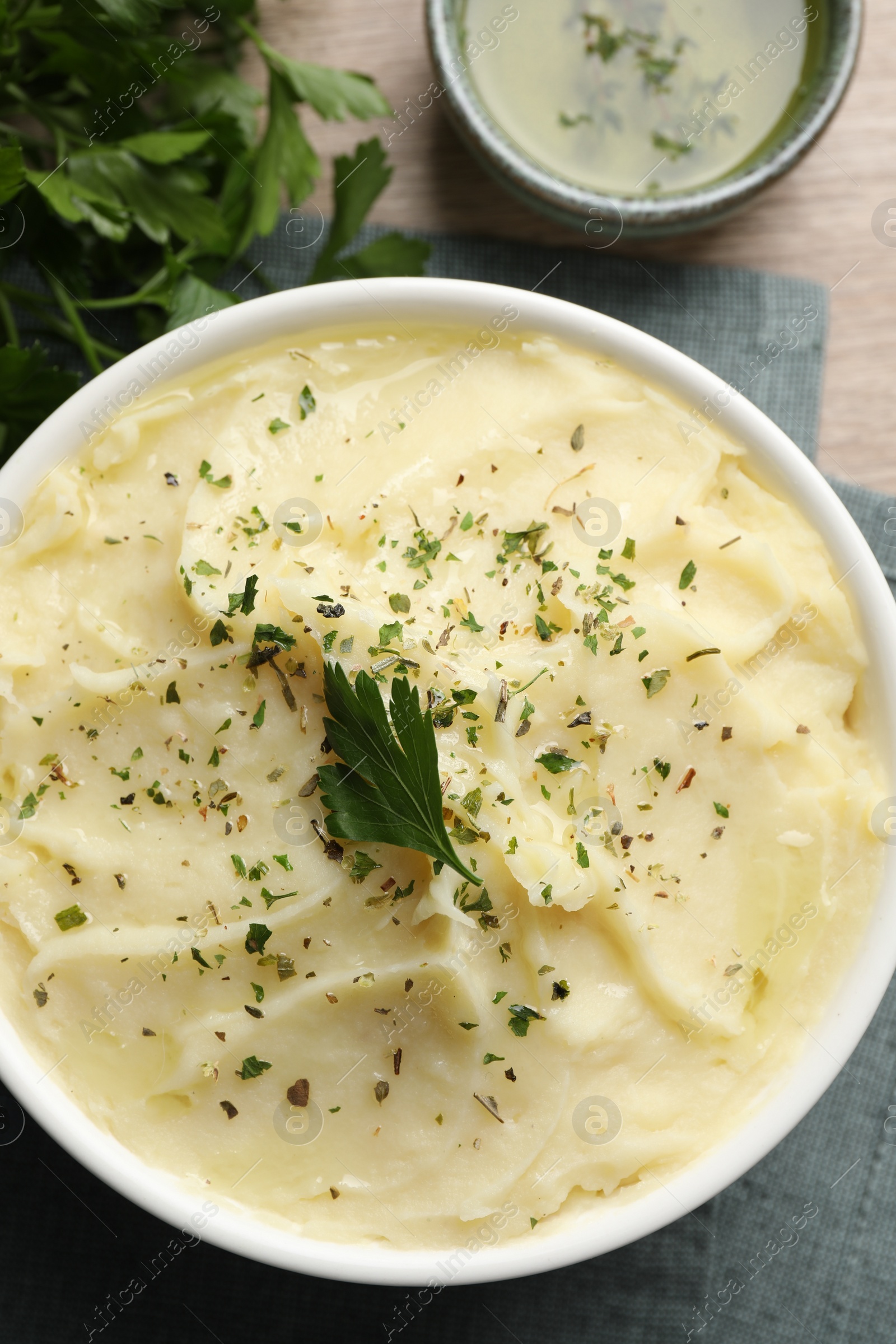 Photo of Bowl of delicious mashed potato with parsley on wooden table, flat lay