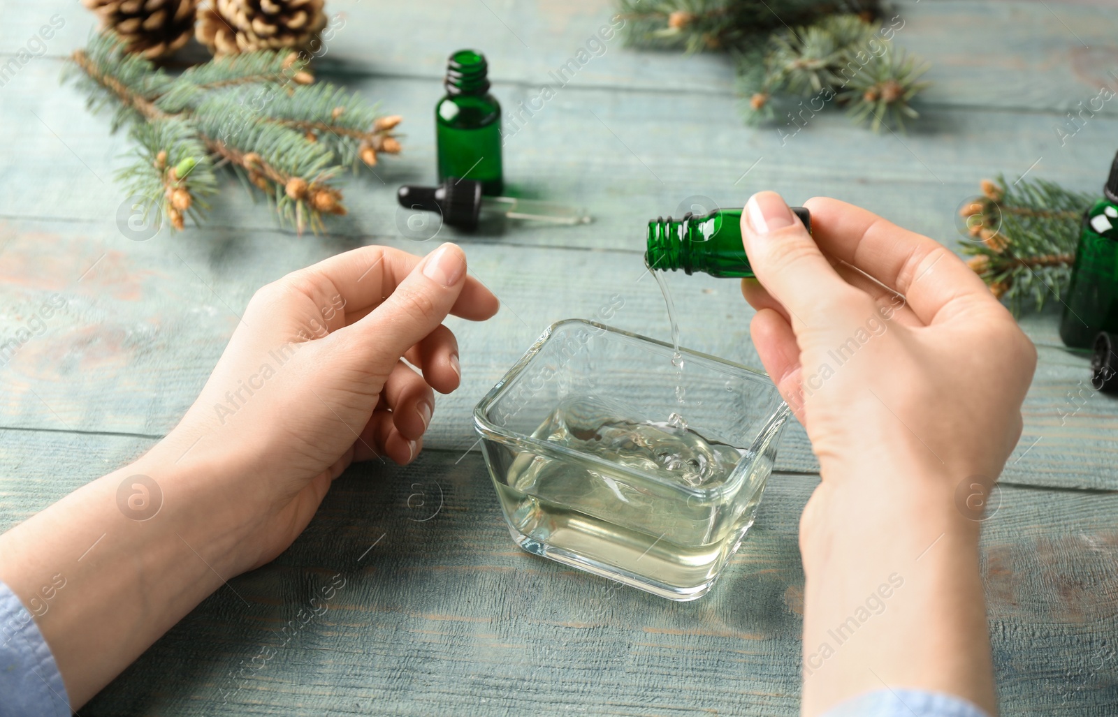 Photo of Woman pouring essential oil into bowl from bottle at table, closeup