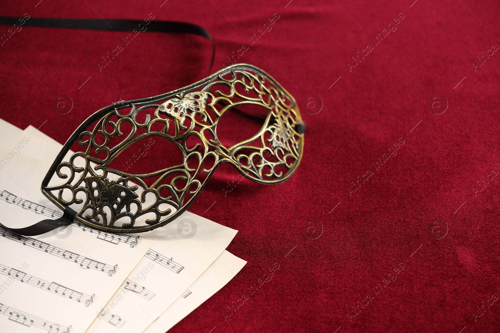 Photo of Elegant face mask and music sheets on red fabric, space for text. Theatrical performance