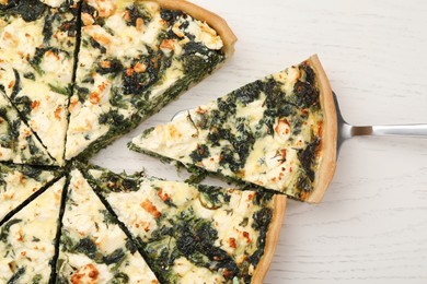 Taking piece of delicious homemade spinach quiche on white wooden table, flat lay