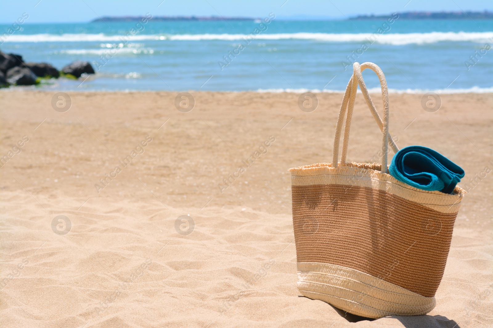 Photo of Soft blue towel in beach bag on sand near sea, space for text